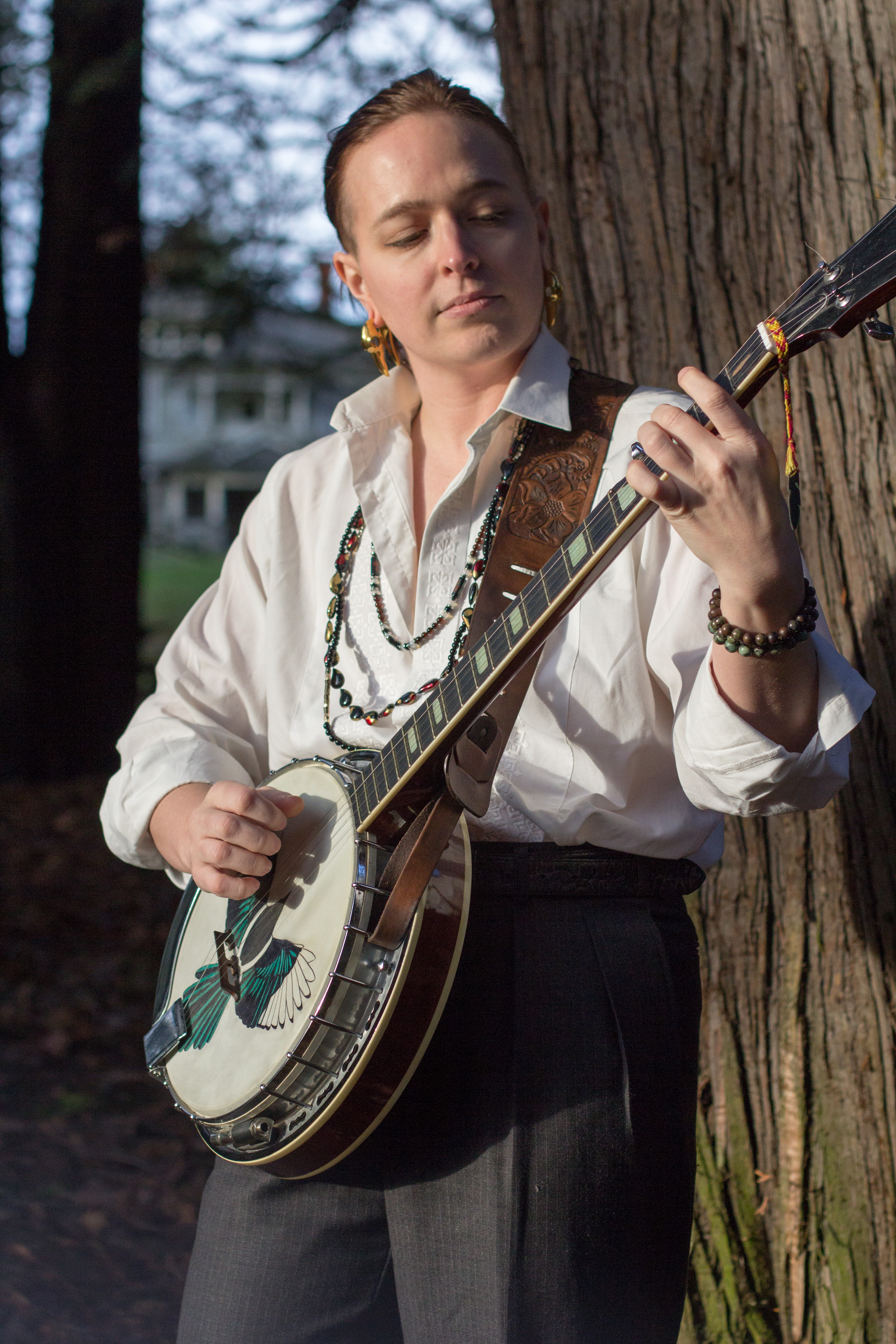 Photo of Dominic playing banjo in front of a tree.